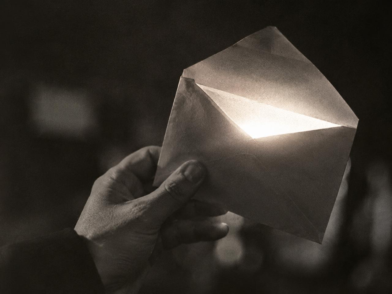 A hand holding an envelope with light pouring out